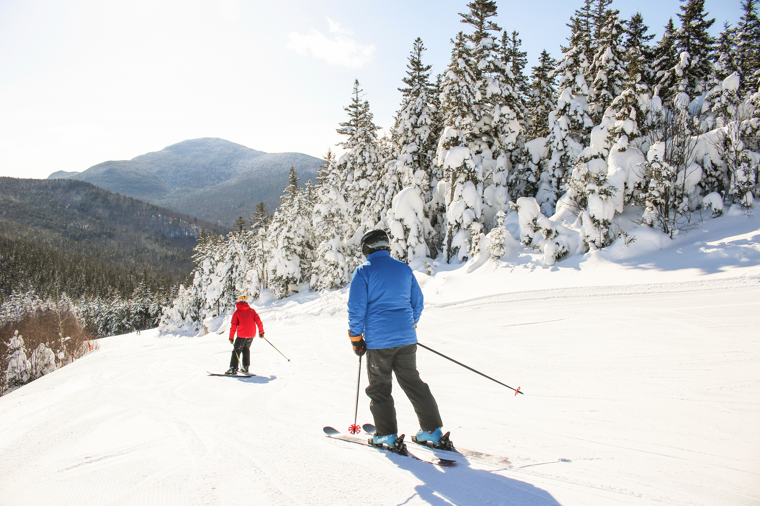 Two skiers glide down a snowy slope on a bright, sunny day at Bretton Woods.