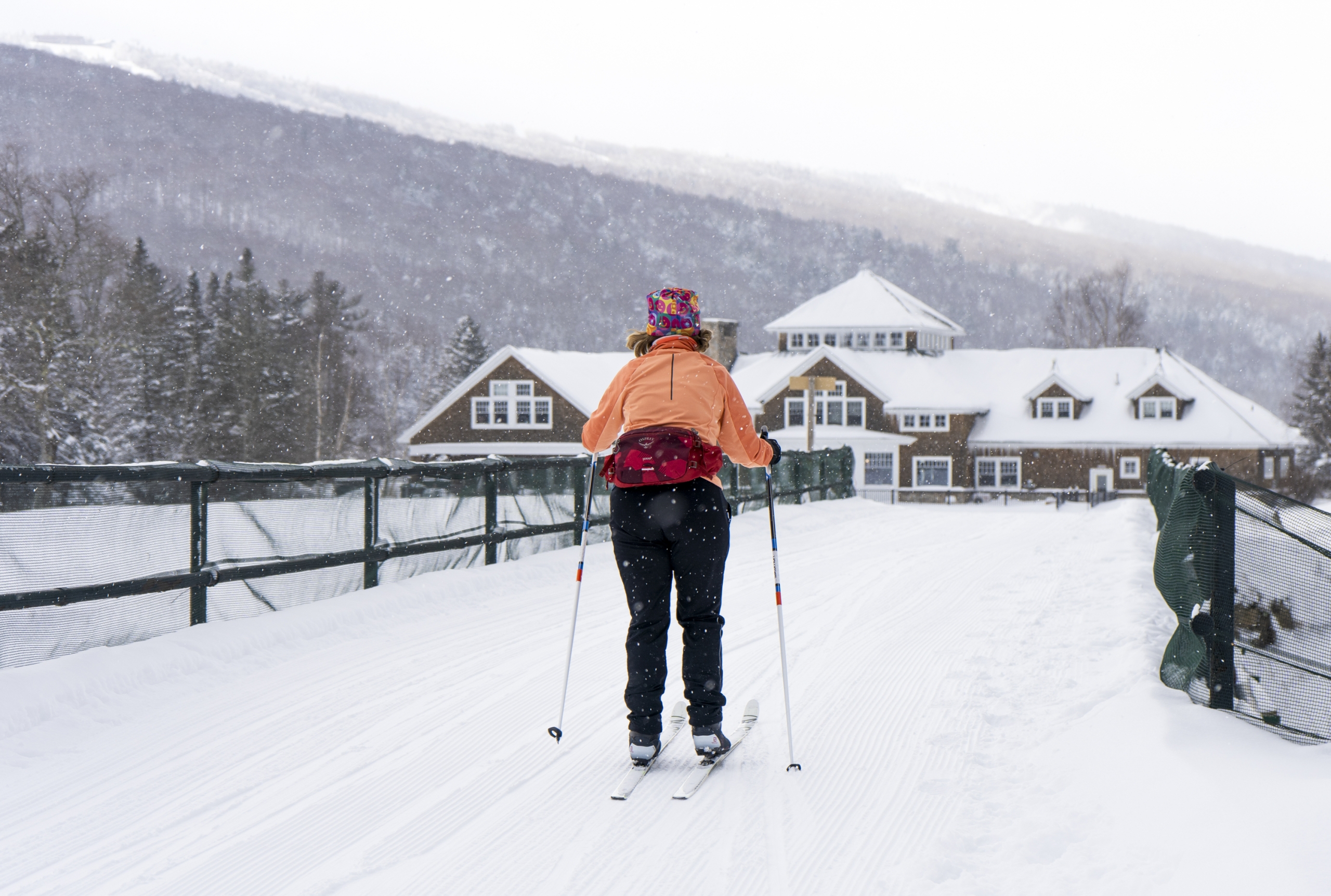 A person cross-country skiing across a snowy bridge toward the ski lodge at Bretton Woods.
