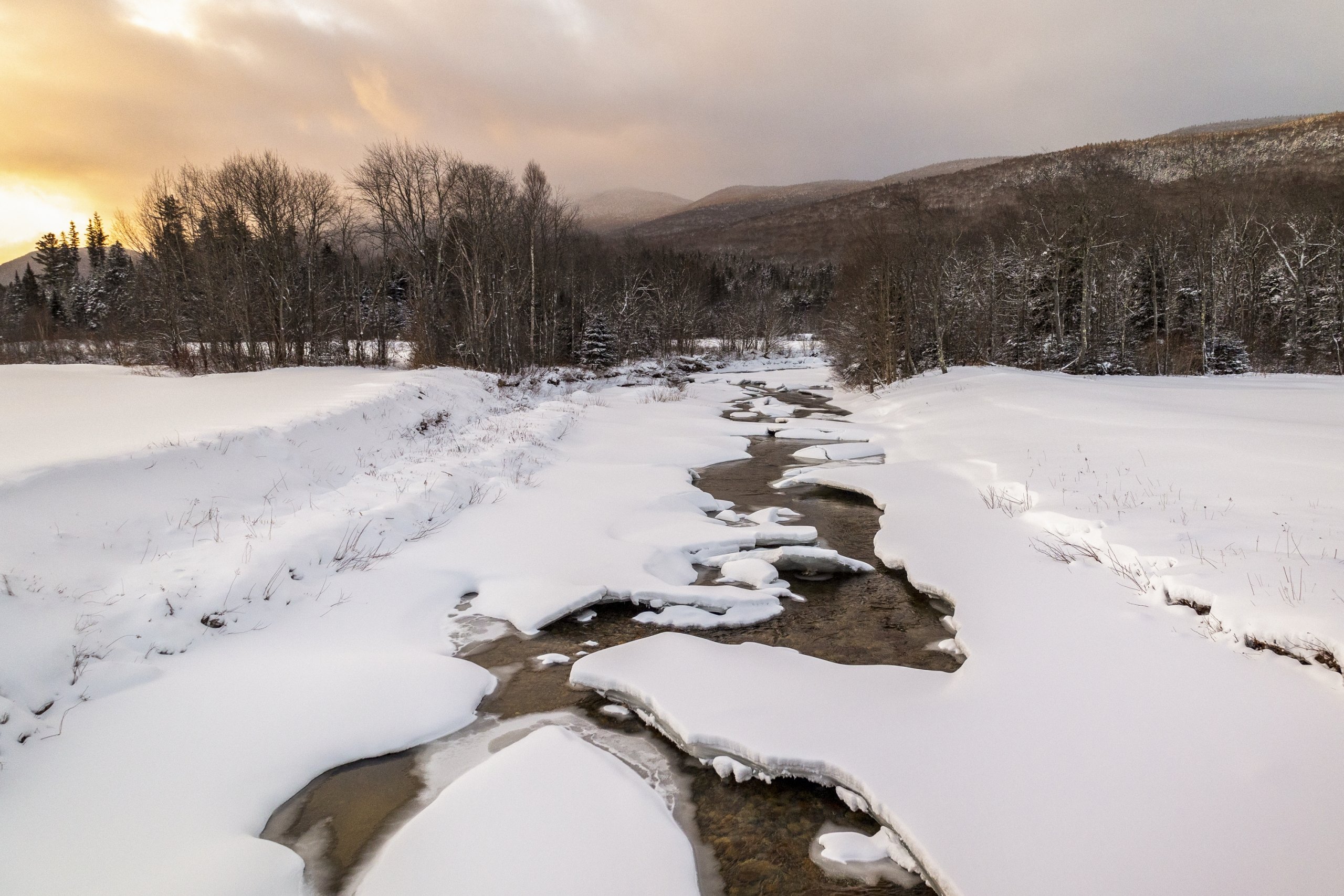 A frozen river runs beside the Nordic trails at Bretton Woods at sunset.