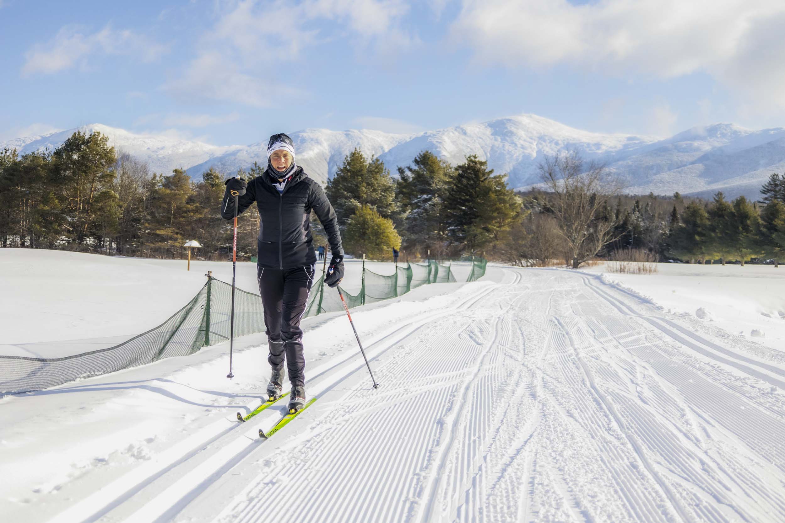 A cross-country skier on a well-groomed track at Bretton Woods, with snow-covered fields and mountains in the background.