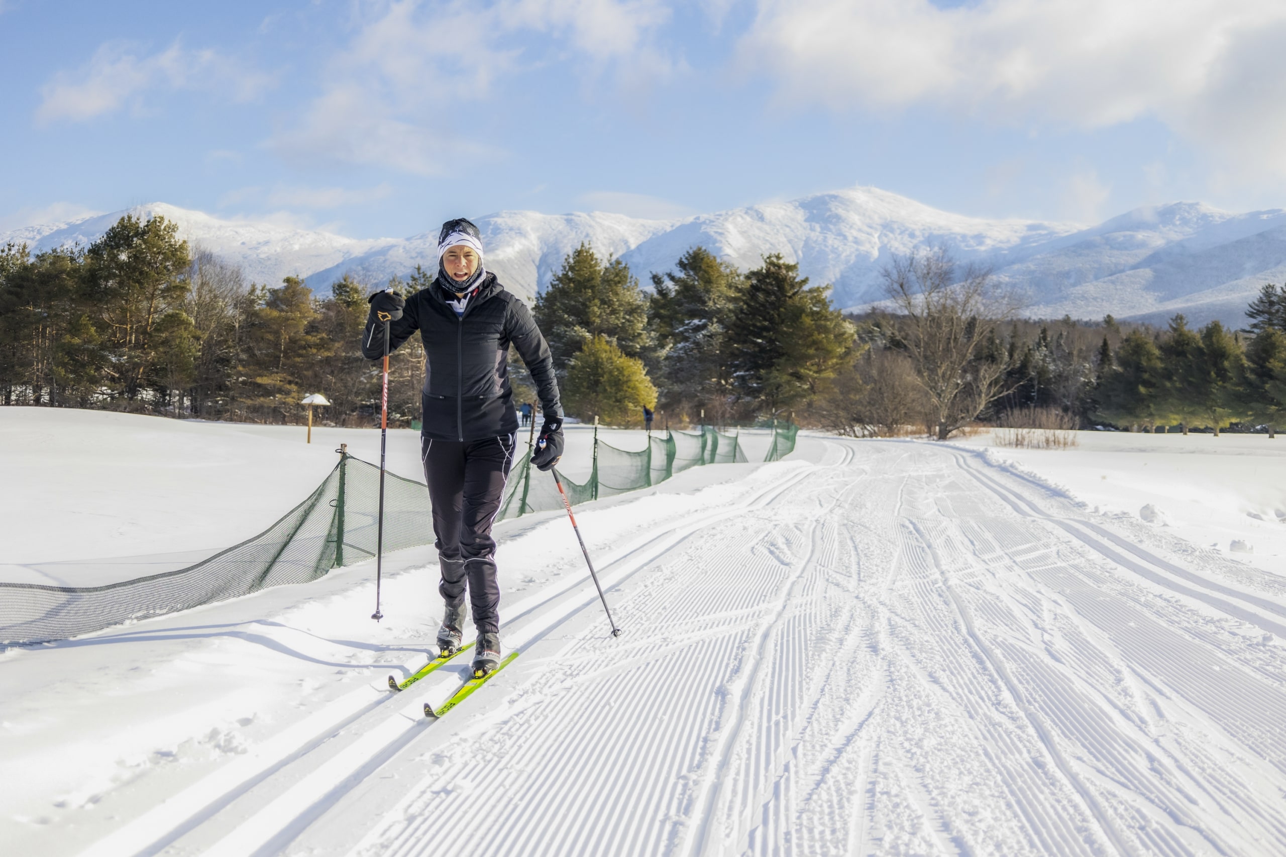 A cross-country skier on a well-groomed track at Bretton Woods, with snow-covered fields and mountains in the background.
