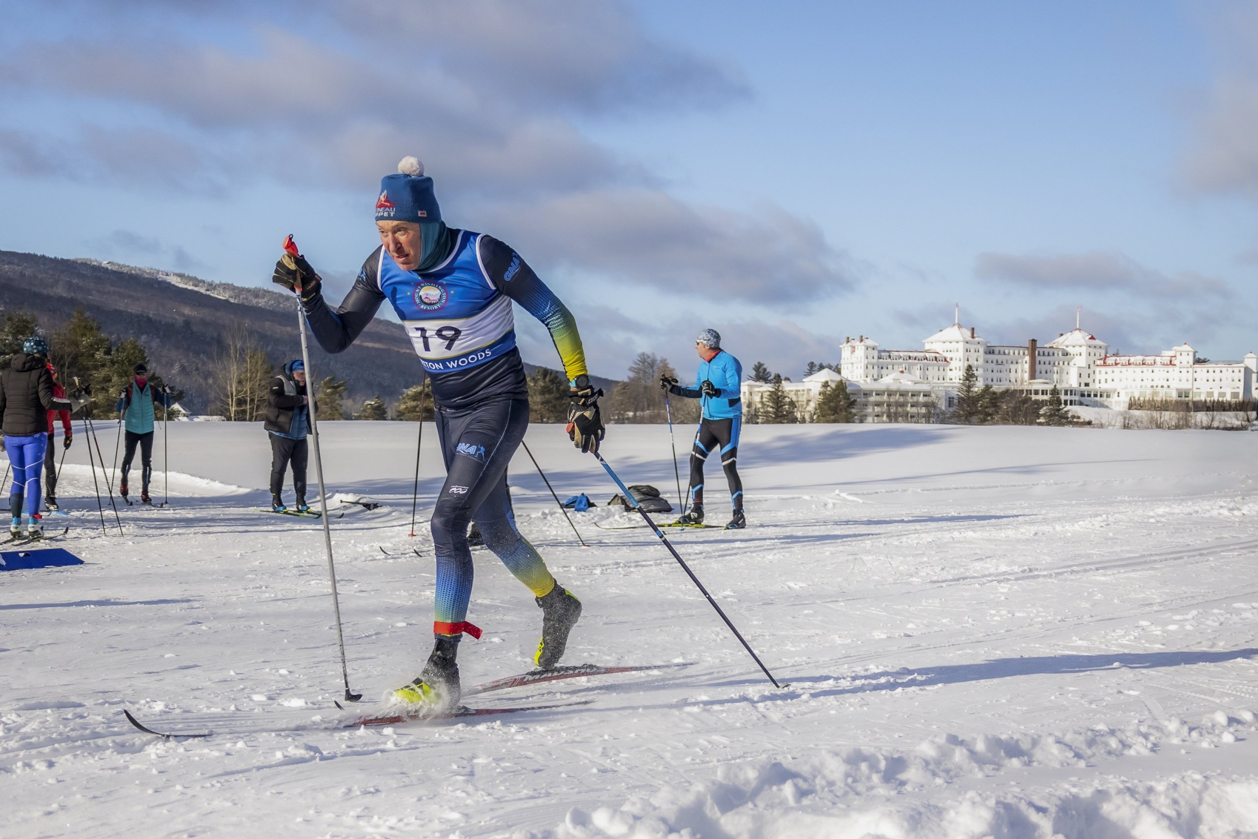 A Nordic skier in racing gear along a trail at Bretton Woods, with Mount Washington Resort and Spa in the distance.