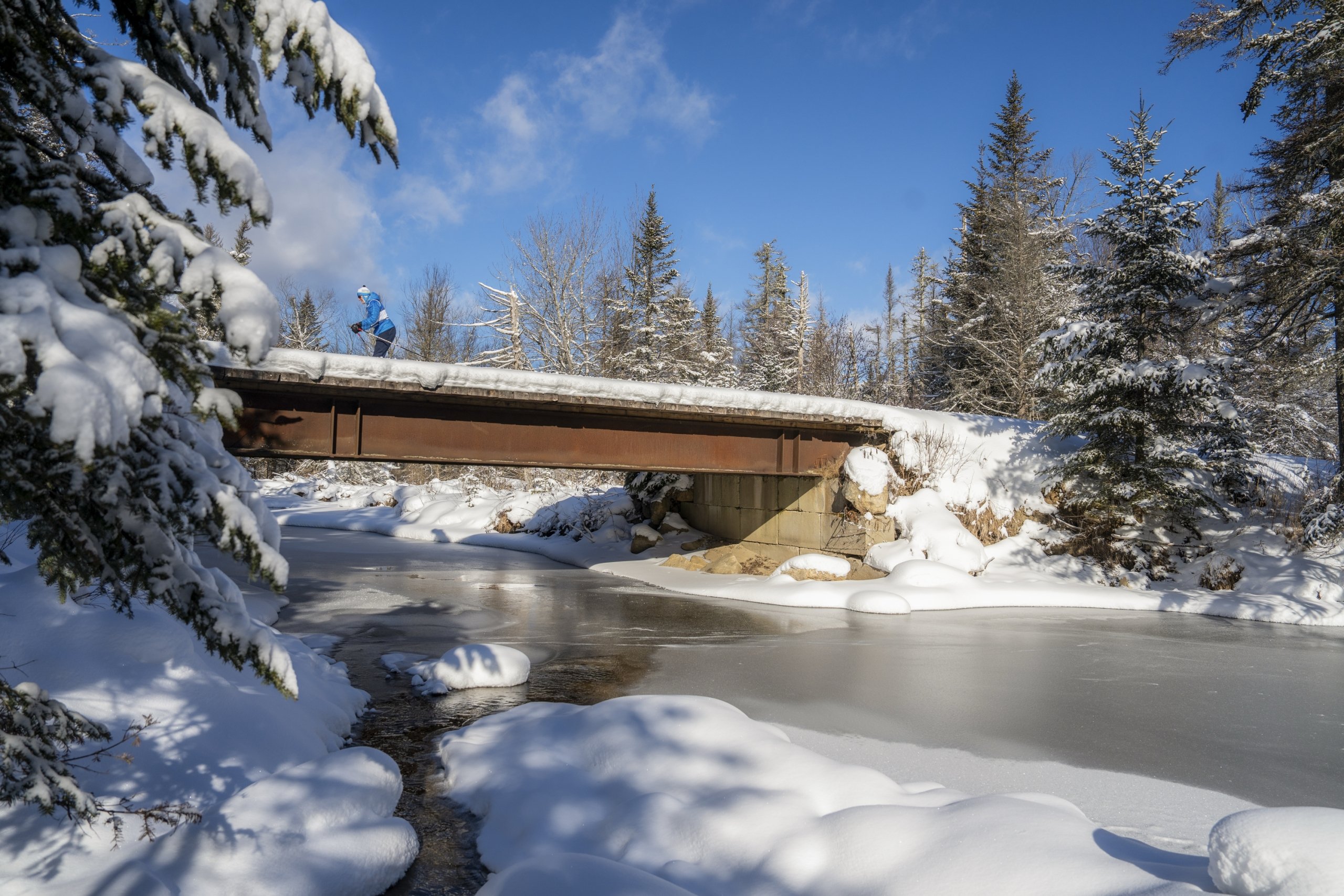 A skier crosses a snowy bridge on Nordic trails at Bretton Woods.