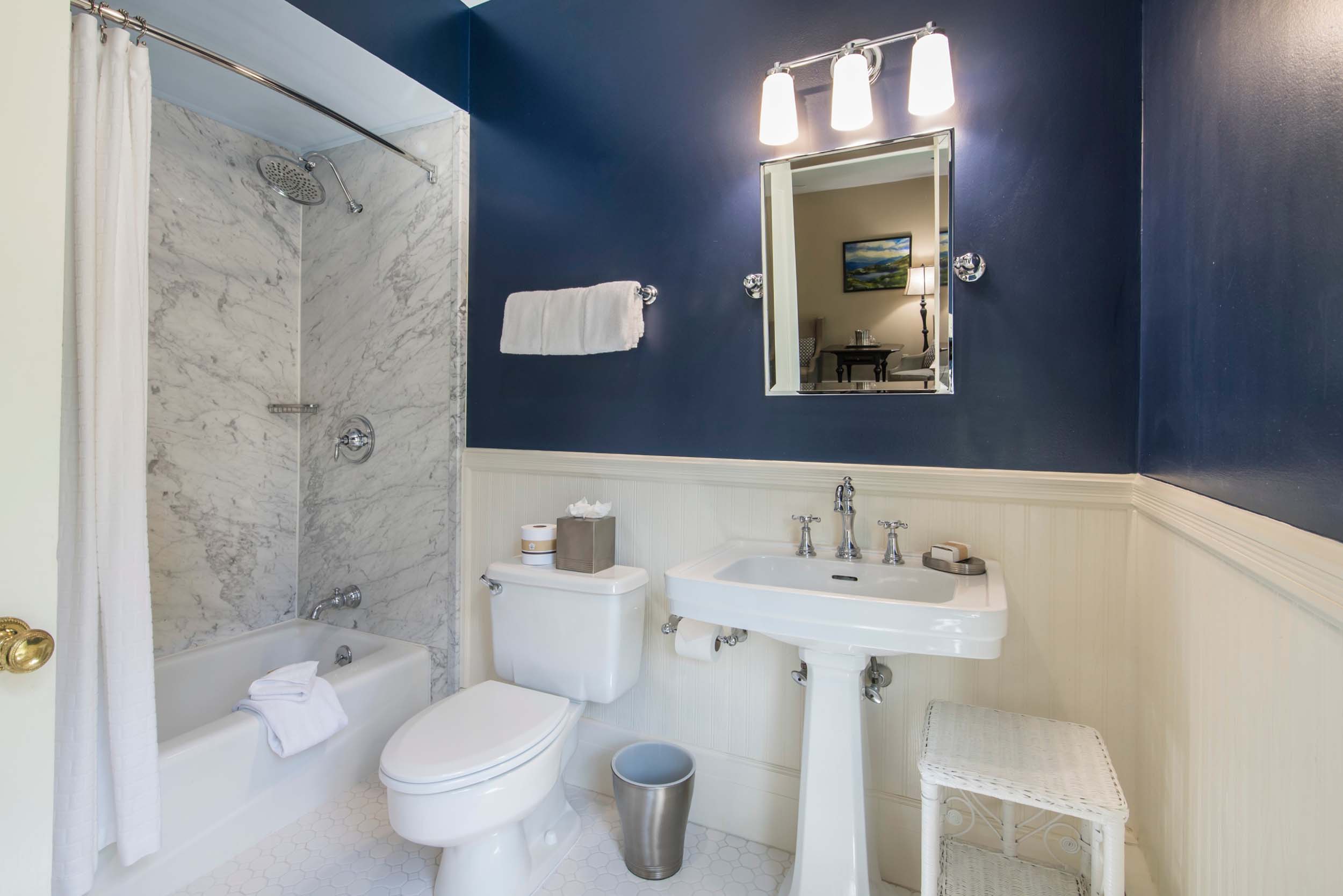 A bright bathroom with navy blue walls, marble shower, and white fixtures at Bretton Arms Inn.