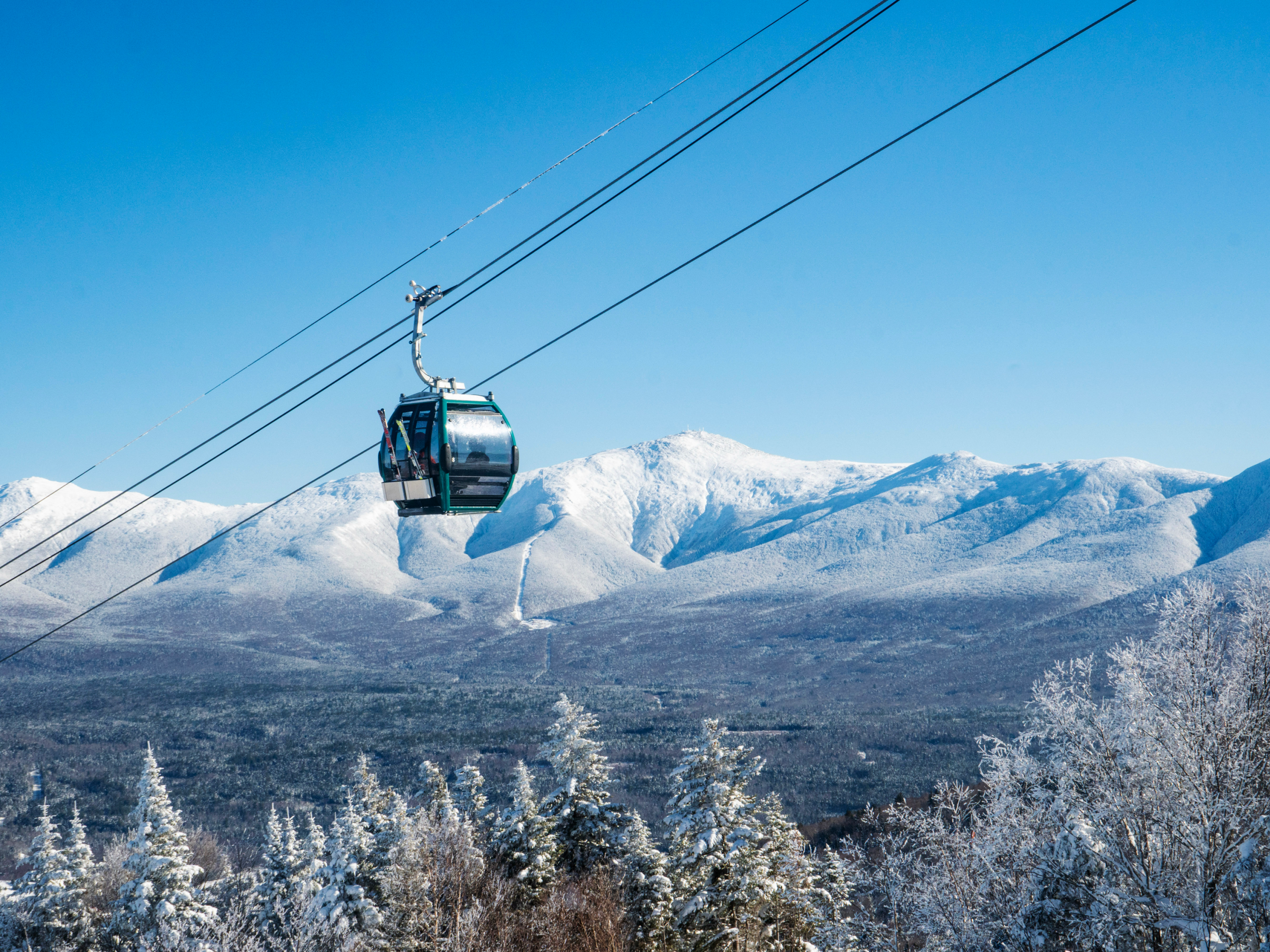 Bretton Woods Gondola over snowy terrain on blue bird day with Mount Washington in the background.