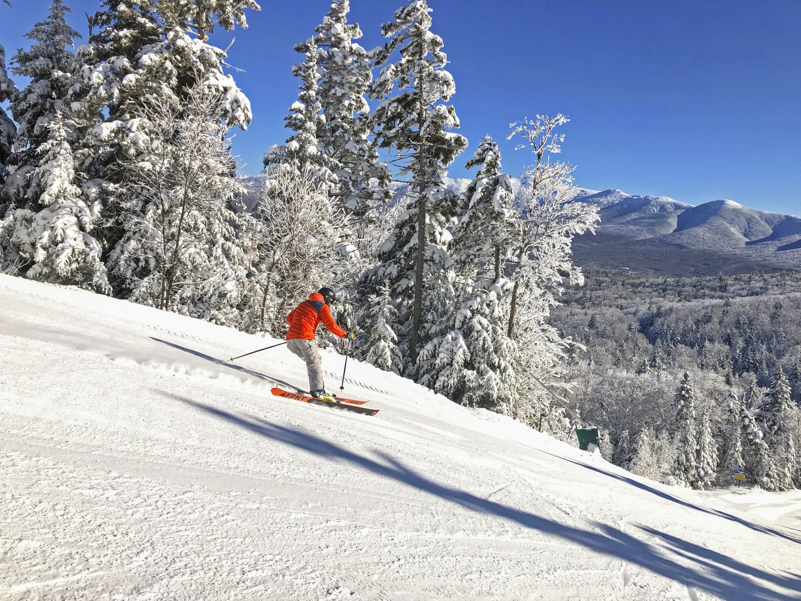 A skier glides down a snowy slope at Bretton Woods with a view of distant mountains.
