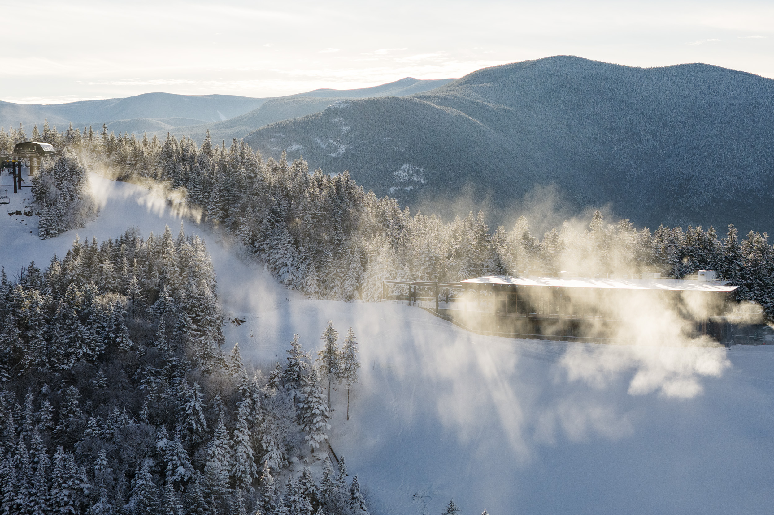 Drone shot at the summit of Bretton Woods with snowmaking backlit by the sun.
