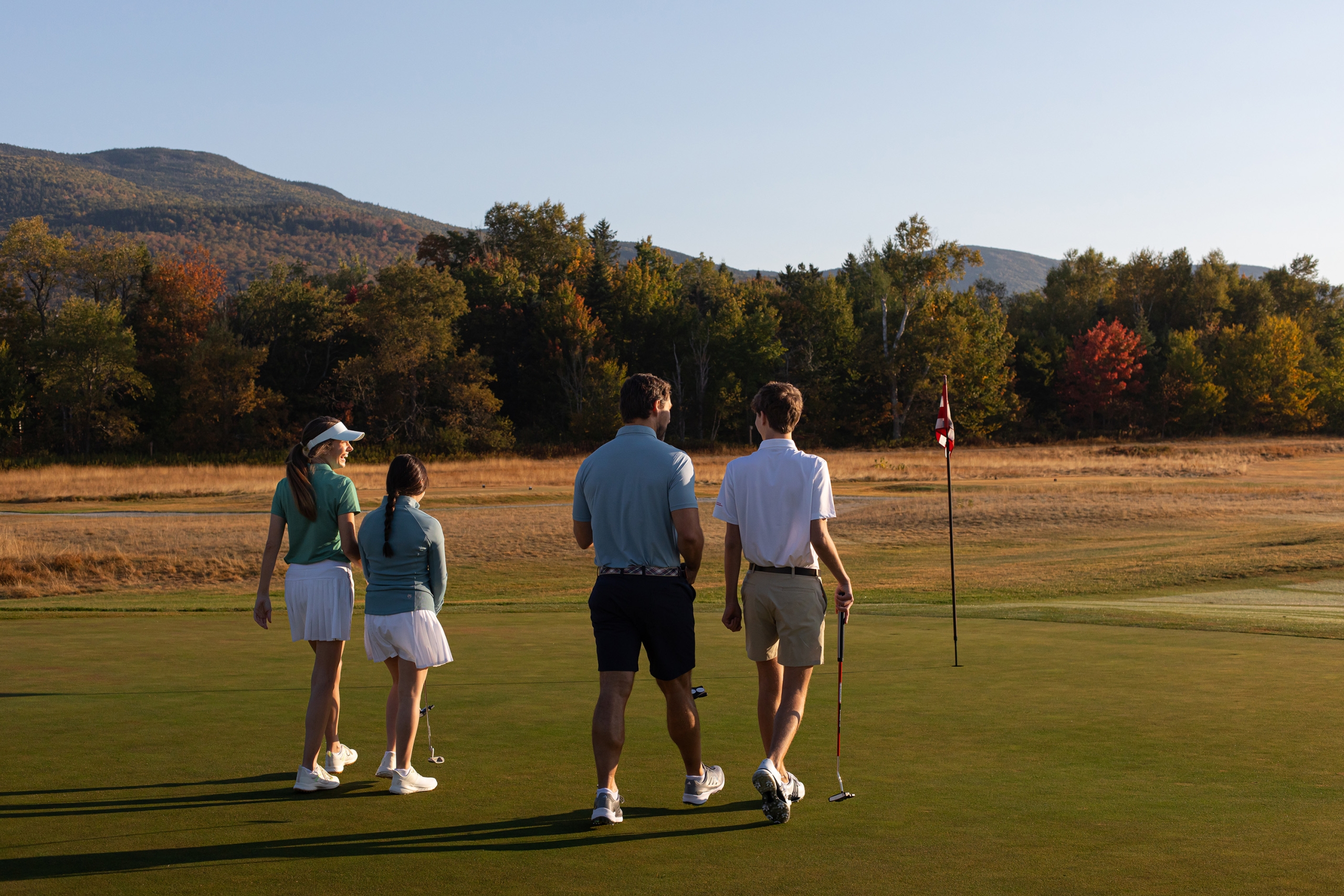 Family of four walking out onto the green during a round of golf on the Mount Washington Course on a late summer morning.