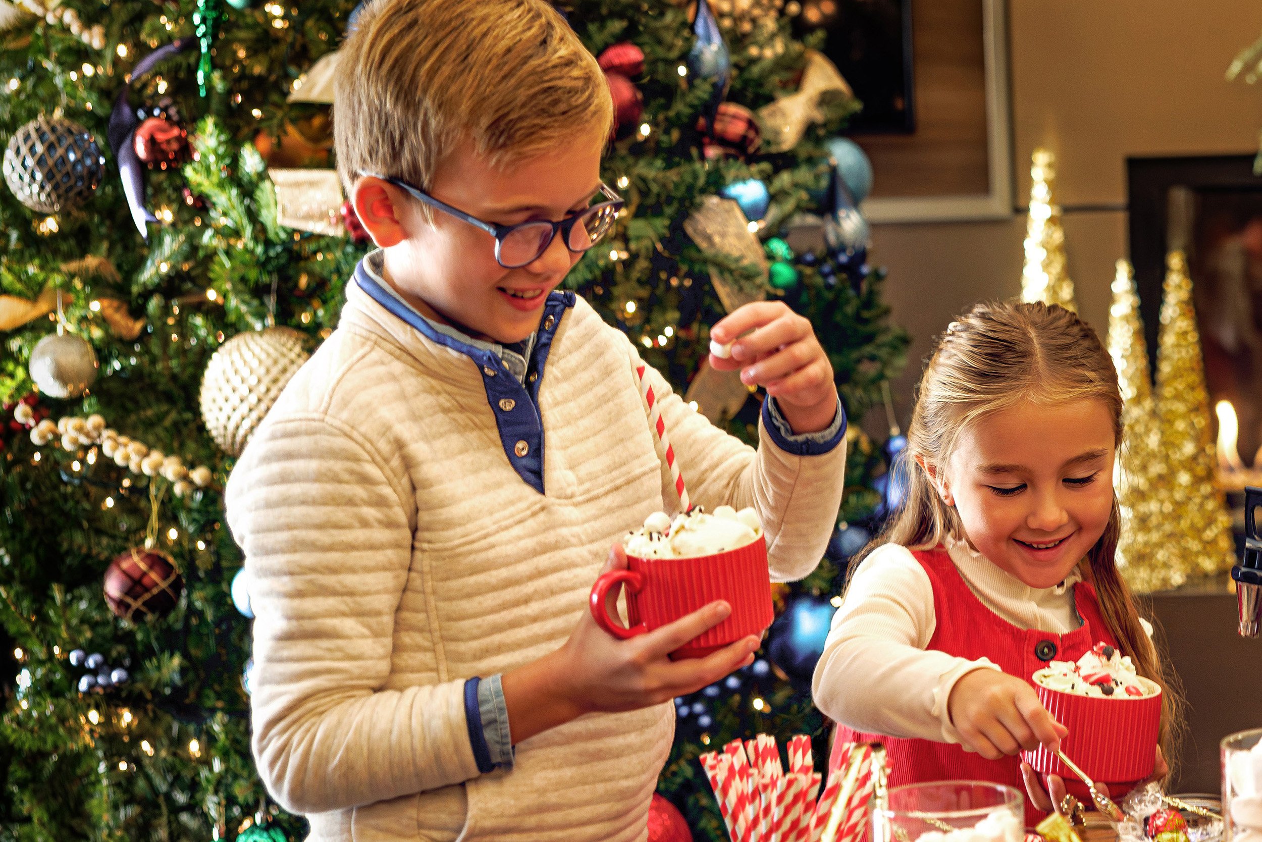 Two kids building hot cocoa in mugs around a festive lobby