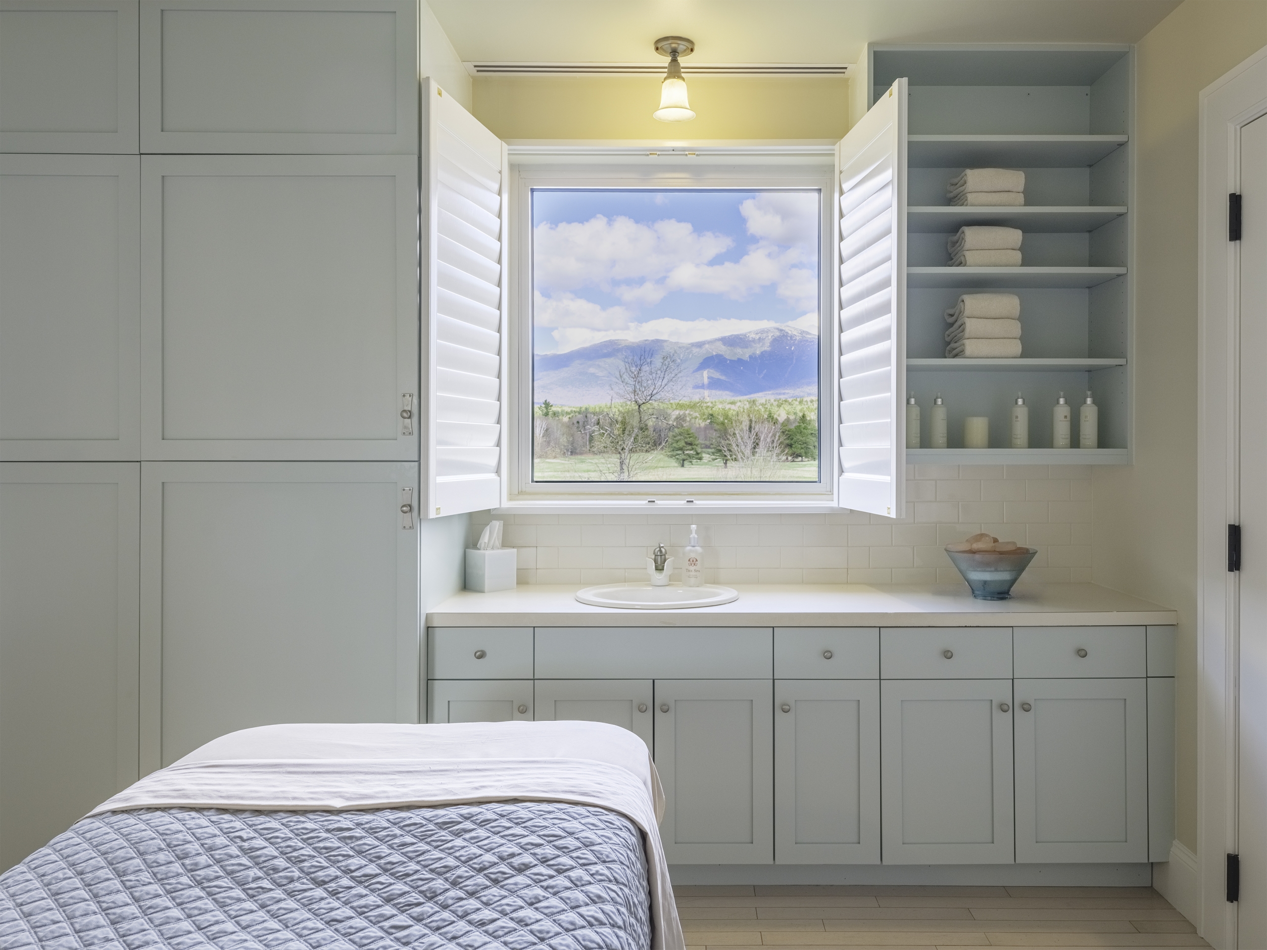 Elegant spa treatment room with a massage table, soft lighting, and a bath robe hung on the wall at Mount Washington Resort and Spa.